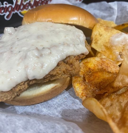 Hand Battered Country Fried Steak Sandwich Topped With Country Gravy on A Brioche Roll Served With Chips.